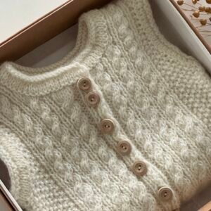 Handgestrickte Baby-Weste mit Zopfmuster und Holzknöpfen in Naturweiss
