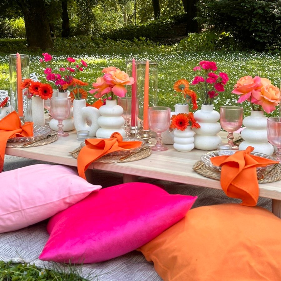 Buntes Picknick-Setup mit Tischdekoration, Blumen und Kissen im Freien